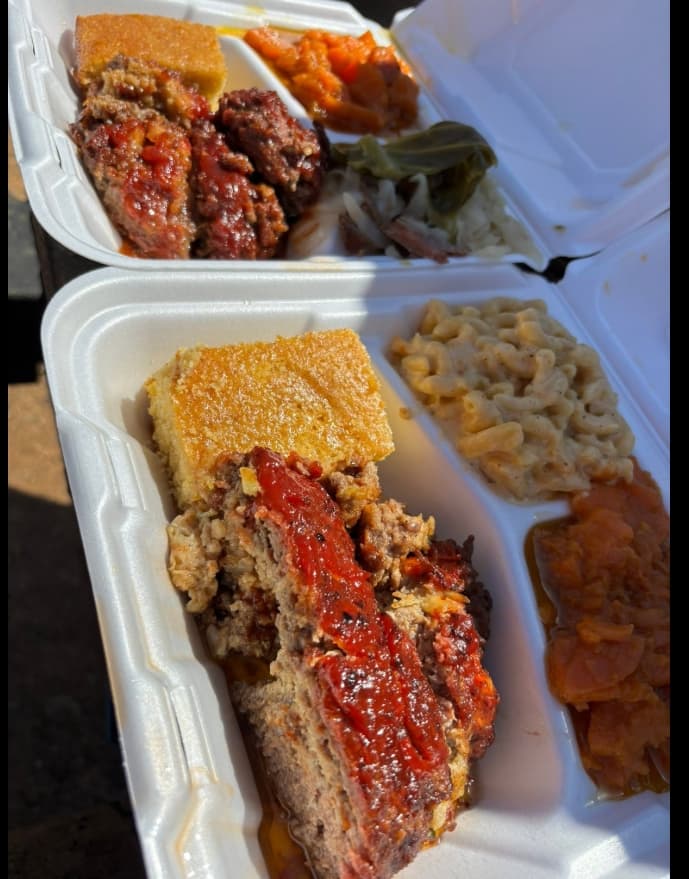 Two plates of glazed meatloaf with cornbread, mac and cheese, greens, and yams