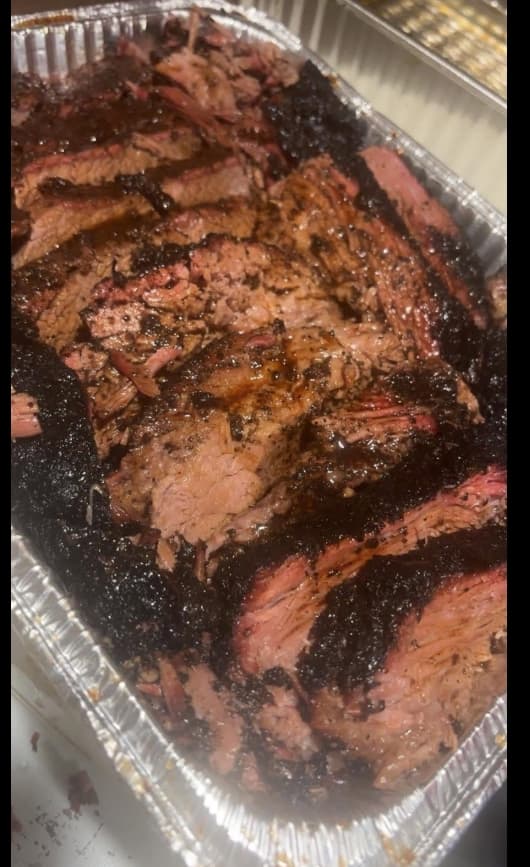Sliced hardwood-smoked beef brisket with heavy bark in a serving pan